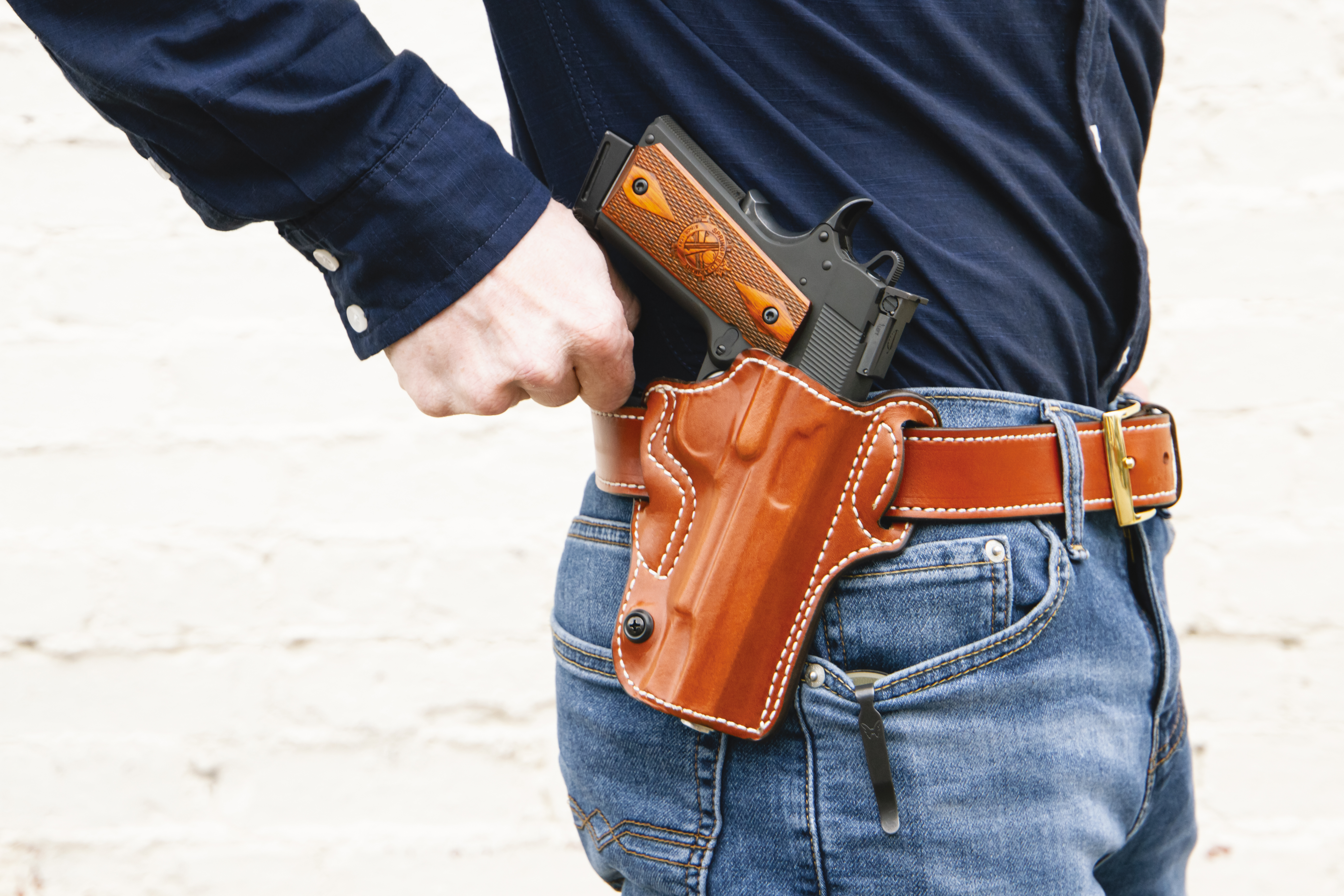 A side view of a man's midsection. He is wearing a black shirt, jeans, and a 1911 holster attached to his belt.