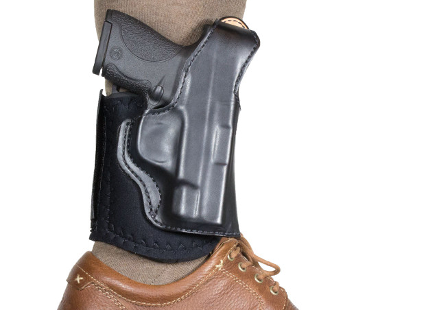 Close-up view of an ankle carry holster holding a handgun around a person's lower leg above the shoe.