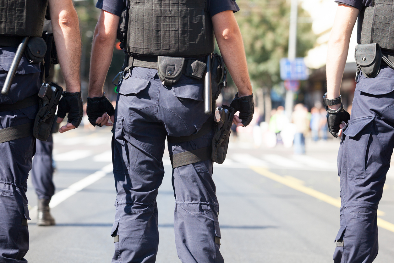 Group of uniformed law enforcement officers wearing duty belts with holsters and tactical gear while walking outdoors. The image shows duty holsters positioned on the officers' belts for professional carry.
