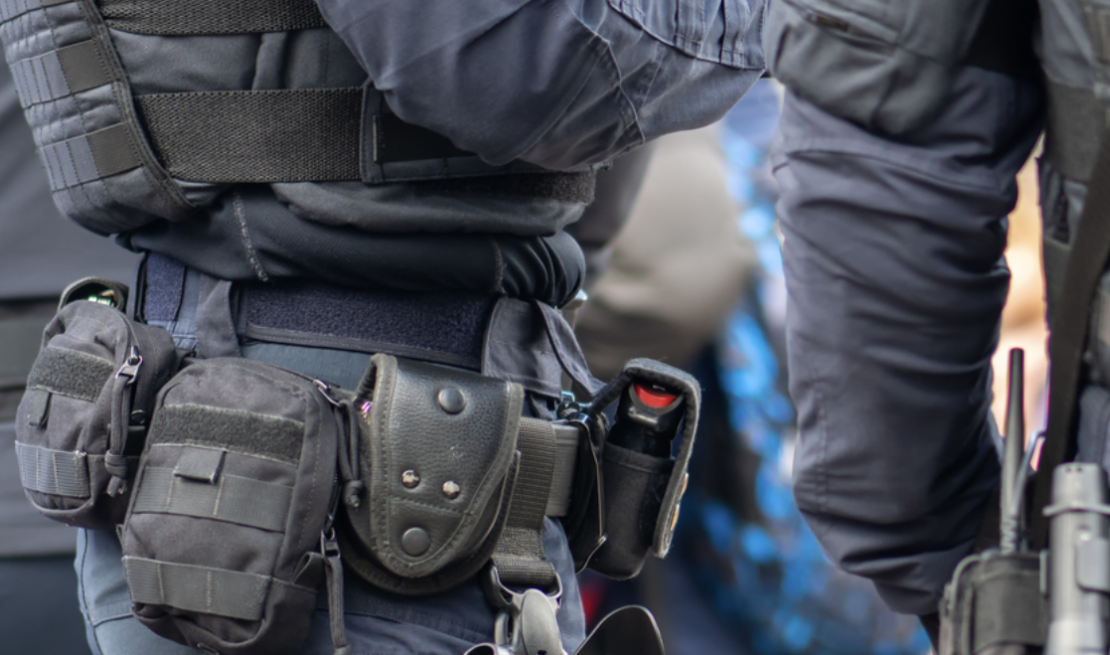 Close-up image of a law enforcement officer wearing a tactical duty belt with pouches, equipment holders, and gear attached around the waist.