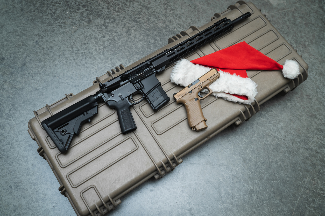 Rifle and handgun displayed on a hard gun case with a red and white Santa hat, representing holiday gifts for gun lovers.