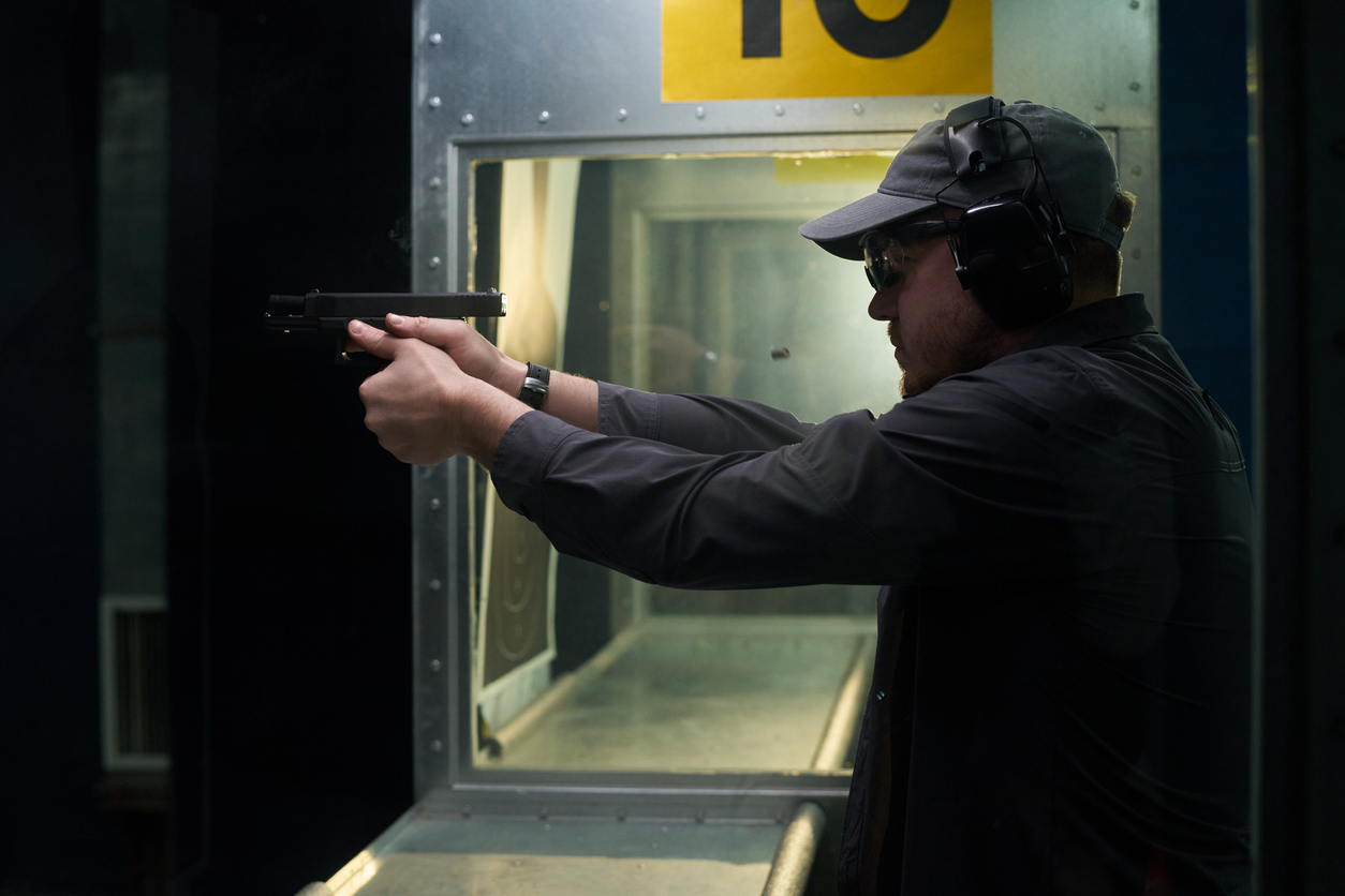 Person wearing eye and ear protection holding a handgun with a two-handed grip at an indoor shooting range.