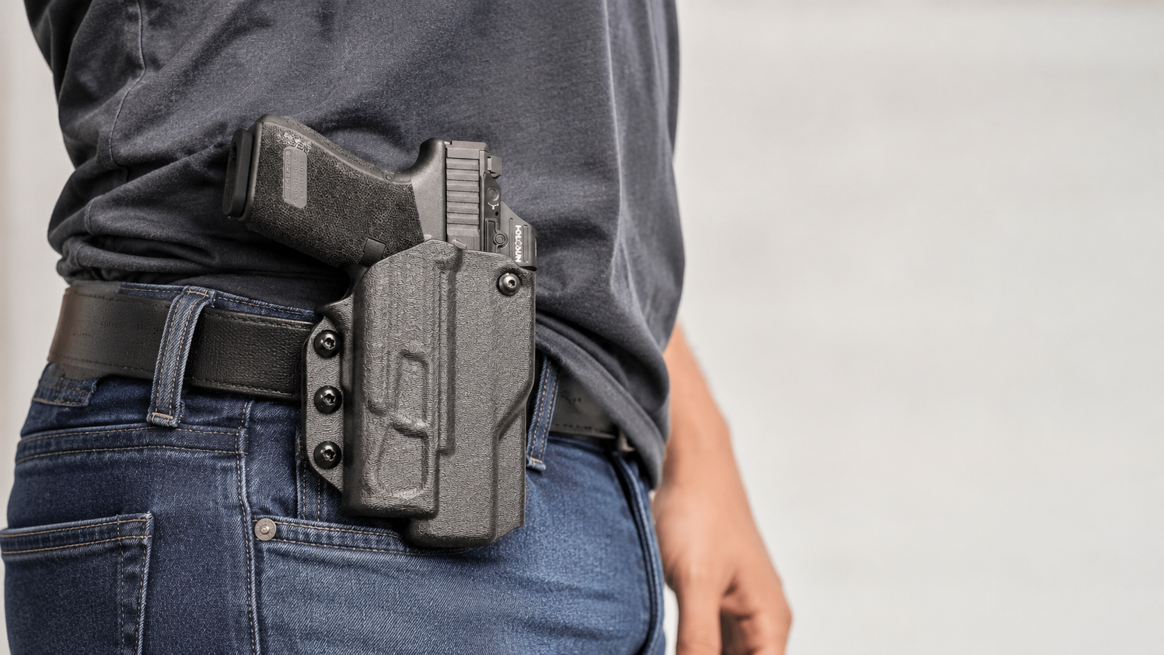 Close-up image of a person wearing a black Level 3 holster with a handgun secured at the waist, showing the holster attached to a belt over jeans.