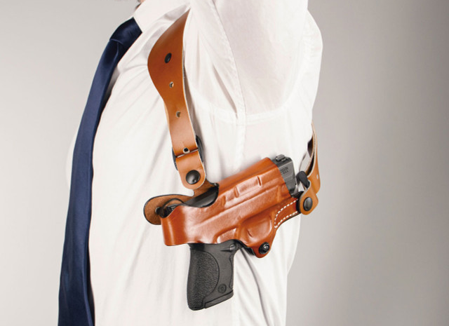Person wearing a shoulder carry holster with a handgun secured under the arm and attached to shoulder straps.